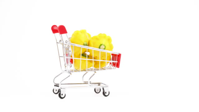 Supermarket-trolley.-Shopping-cart-with-yellow-pattypan-squashes.-Moving-in-the-frame.-Isolated-on-the-white-background.-Close-up.-Macro.