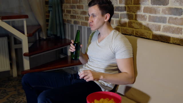 Man-drinks-beer-and-chips-in-front-of-TV-watching-football