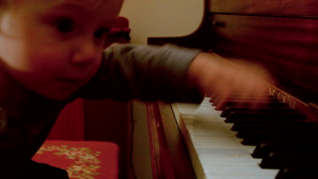 Caucasian-Toddler-Boy,-Sitting-at-a-Piano-with-Him-Mom,-Plays-on-the-Piano-with-a-decorated-Christmas-Tree-Behind-Them