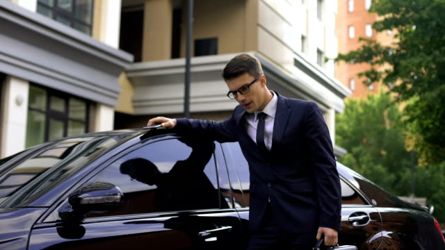 Upset-young-businessman-standing-near-luxurious-car,-talking-on-phone,-bad-news