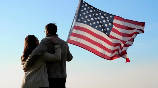 Patriotic-family-with-a-large-flag-of-America-in-hand-outdoors