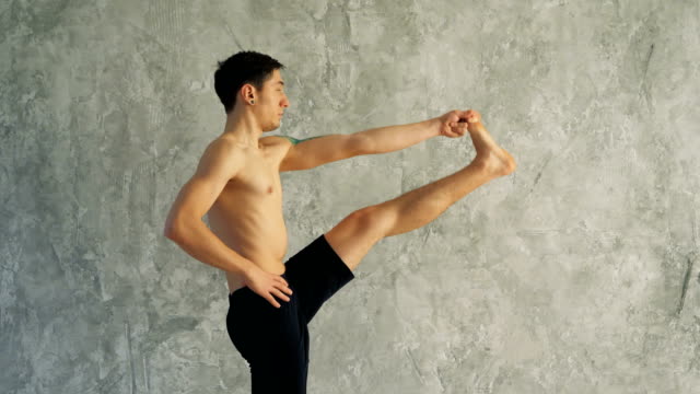 Sportsman-doing-sport-exercise,-bending-in-variation-of-Utthita-Hasta-Padangusthasana,-Dandayamana-Janushirasana,-Standing-Head-to-Knee-Bikram-posture