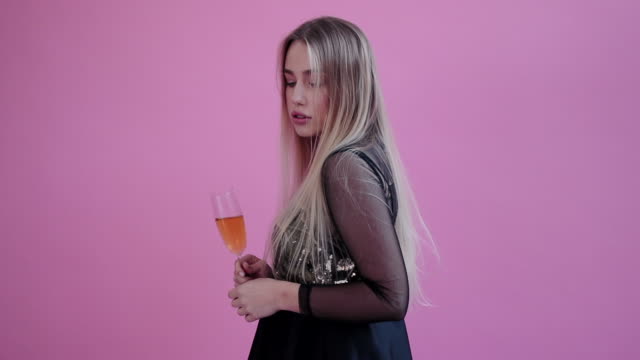 Hübsches-Mädchen-tragen-rote-Hörner,-halten-Sie-ein-Glas-Champagner-und-für-Kamera-im-Studio-rosa-Hintergrund-darstellen