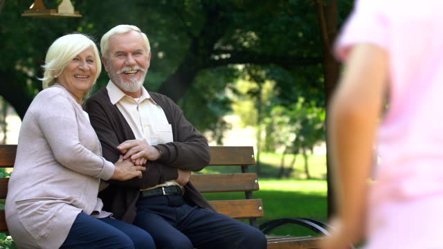 Old-couple-sitting-on-bench-and-happily-watching-their-grandchildren-having-fun