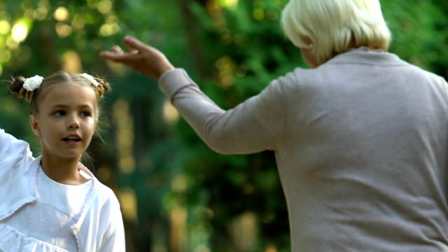 Little-active-girl-emotionally-talking-to-granny-while-walking-in-park,-family
