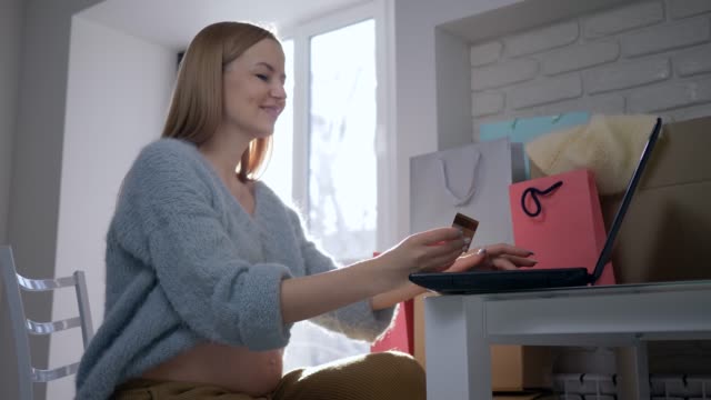Internet-payment,-beautiful-expectant-female-with-credit-card-uses-laptop-computer-for-online-purchases-on-Internet