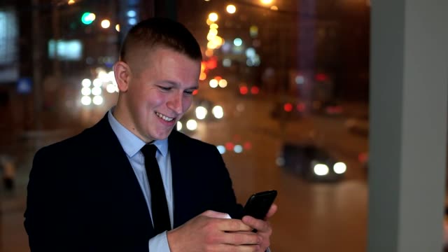 The-man-businessman-looks-at-the-smartphone-happy,-happy.-Outside-the-window,-against-the-night-city.