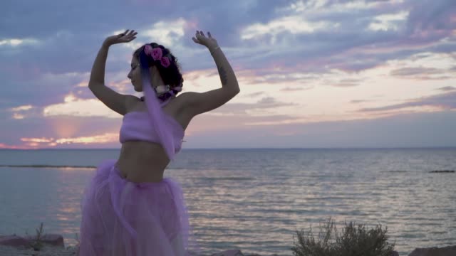 Cute-woman-with-sparkling-makeup-in-a-pink-dress-dancing-on-the-bank-of-the-river.-The-dance-of-a-sensual-girl-with-a-wonderful-hairstyle-with-flowers.-Slow-motion.