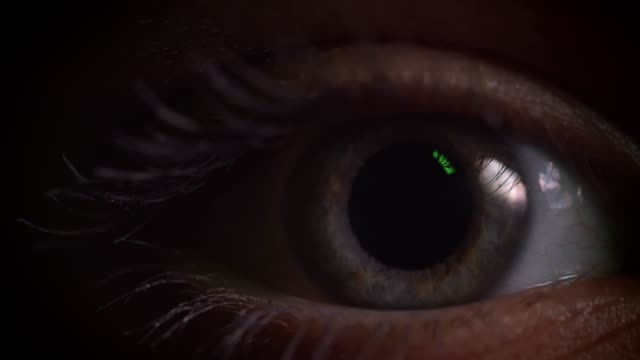 Close-up-shoot-of-gray-eye-blinking-with-reflection-of-green-lamp-on-it-in-complete-darkness.