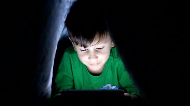 Kleiner-Junge-lesen-Buch-auf-digitalen-Tablet-in-der-Nacht