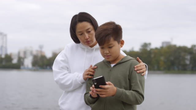Asiatische-Mutter-und-Sohn-mit-Workout-App-auf-Smartphone-im-Freien