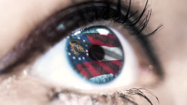 Woman-blue-eye-in-close-up-with-the-flag-of-Georgia-state-in-iris,-united-states-of-america-with-wind-motion.-video-concept