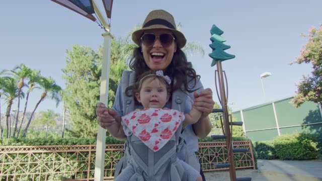 POV-coming-down-on-slide-at-park-to-meet-mother-with-baby-on-carrier