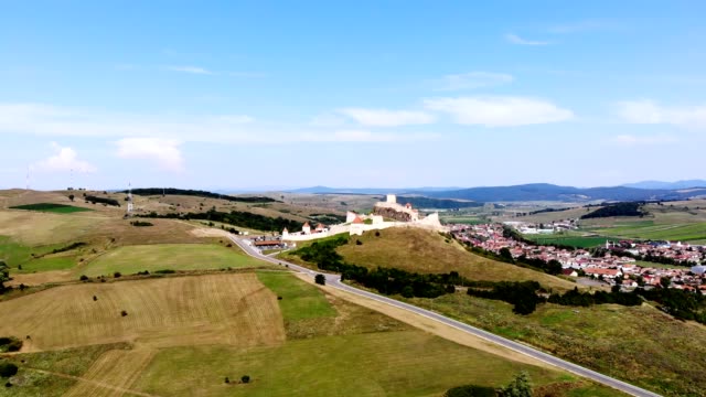 aero.-panoramic-view-of-the-ancient-castle,-Rupea-defense-fortress-placed-on-top-of-a-hill.-at-the-foot-of-castle-there-is-a-small-town.-Transylvania,-Romania.-sunny-hot-summer-day