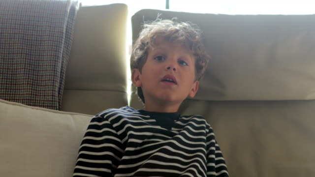 Child-face-trying-to-watch-television-screen-in-4K.-Young-boy-seated-in-sofa-starring-and-wanting-to-see-something-behind-viewer