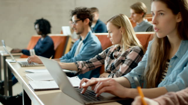 En-el-aula-Multi-étnica-estudiantes,-uso-ordenadores-portátiles-mientras-escuchando-a-un-profesor.-Algunos-escriben-en-cuadernos.-Brillantes-jóvenes-estudio-en-la-Universidad.