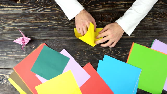 Male-hands-folding-yellow-paper-sheet.