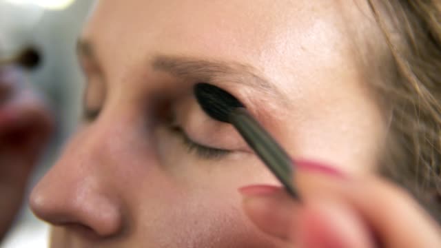 Extremely-close-of-a-young-woman's-face.-Make-up-artist-putting-on-nude-eyeshadows-using-two-brushes-at-the-same-time