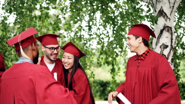 Begeisterte-junge-Männer-und-Frauen-Absolventen-machen-High-Five,-umarmen-und-lachen-halten-Diplome-feiern-Abschlusstag.-Emotionen-und-Erfolgskonzept.