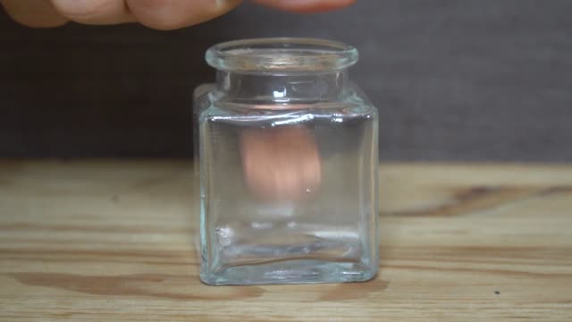 Business-concept---man-hand-throw-euro-coins-into-little-transparent-jar.