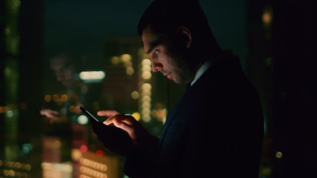 Spät-abends-im-Büro-Typen-erfolgreicher-Geschäftsmann-E-Mail-auf-das-Smartphone.-In-der-Ansicht-Fenster-Geschäftsviertel-mit-Citylights.