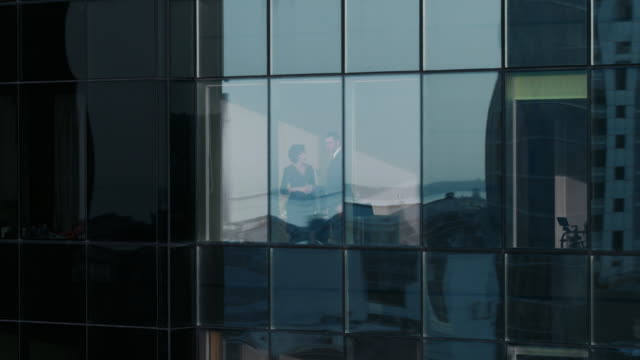 Luftaufnahmen-Footage-von-außerhalb-von-der-Wolkenkratzer:-Geschäftsmann-und-geschäftsfrau-sprechen-Unternehmen-stehen-in-das-Office-Fenster.-Schuss-von-der-finanziellen-Geschäftsviertel-und-Geschäftsleute-arbeiten-in-der-großen-Stadt-fliegen.