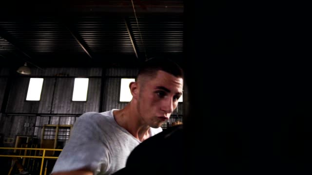 Aufnahmen-von-einem-männlichen-Boxer-trainieren-Sie-im-Fitness-Studio,-Trainingsprozess-mit-Boxsack-hautnah.-Boxer-in-schwarz-Boxhandschuhe,-white-t-shirt
