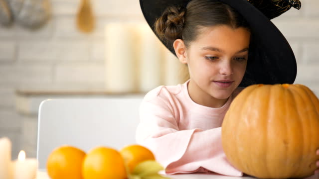 Cute-girl-in-witch-costume-showing-jack-pumpkin-and-smiling,-preparing-for-party