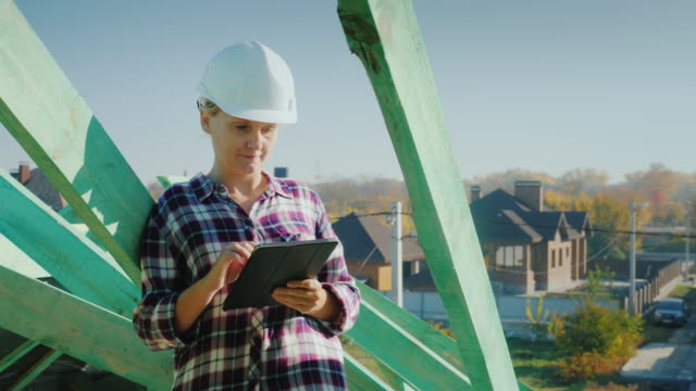 A-female-architect-is-working-with-a-tablet-on-the-roof-of-a-house.-Technical-and-author's-control-in-construction
