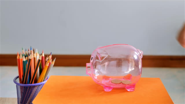 Hand-of-boy-putting-coin-into-piggy-bank.-Saving-for-education-fund-concept