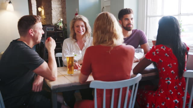Grupo-de-raza-mixta-de-amigos-adultos-jóvenes-sentados-en-una-mesa-en-un-bar-hablando