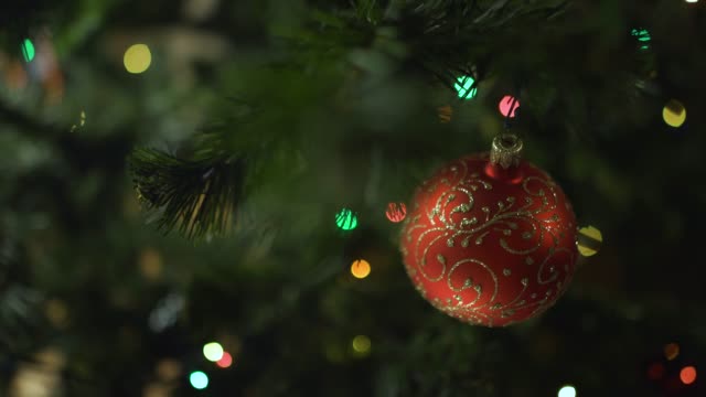 eine-Glas-Spielzeug-hängt-ein-geschmückter-Weihnachtsbaum-vor-dem-Hintergrund-von-blinkenden-Lichtern