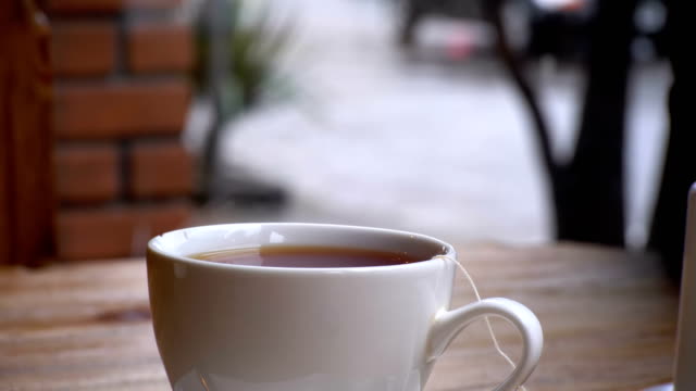 Blanco-taza-de-té-caliente-sobre-la-mesa-en-un-café-en-el-fondo-de-la-ventana-de-la-calle