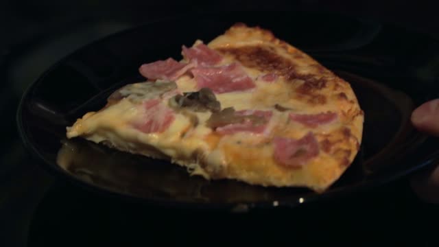 Close-up-a-piece-of-pizza-with-ham,-mushrooms,-and-cheese-on-a-black-plate