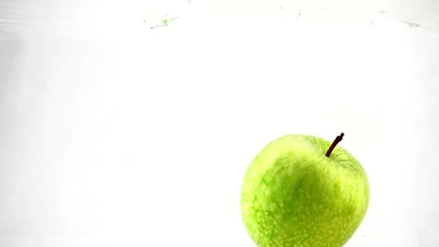 Una-manzana-verde-son-arrojadas-a-un-recipiente-de-agua.-Video-en-cámara-lenta.