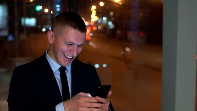 The-man-businessman-looks-at-the-smartphone-happy,-happy.-Outside-the-window,-against-the-night-city.