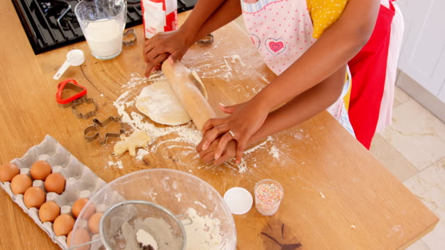 High-angle-view-of-black-mother-and-daughter-rolling-dough-in-kitchen-of-comfortable-home-4k
