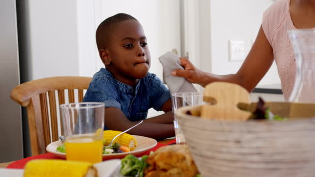 Front-view-of-mid-adult-black-father-wiping-sons-mouth-at-dining-table-in-a-comfortable-home-4k