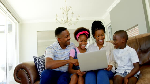 Vista-frontal-de-la-familia-joven-negro-sentado-en-el-sofá-y-usando-la-laptop-en-una-casa-confortable-4k