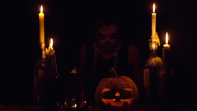 Halloween-Hexe-hält-Messerklinge-mit-Schädel-Make-up-magische-Kürbisketten-und-Kerzen