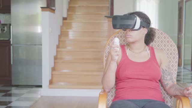 Hübsche-afroamerikanische-Frau-sitzt-auf-dem-Sessel-zu-Hause-in-der-Virtual-Reality-Headset