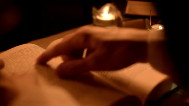 Big-Close-up-girl-magician-in-a-dark-room-with-candlelight-looking-for-a-spell-in-a-book.-Low-key-live-camera.