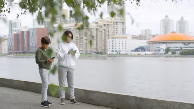 Asiatische-Mutter-und-Sohn-mit-Smartphone-und-Laufen-im-Freien
