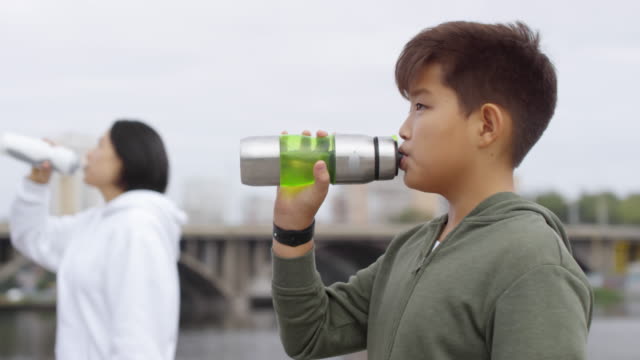 Asian-Boy-Drinking-Water-nach-dem-Laufen-mit-Mutter