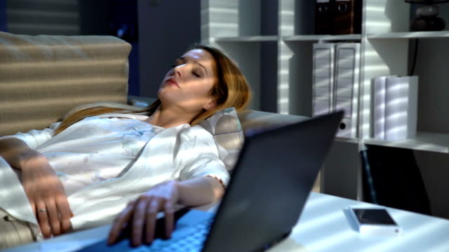 Mujer-de-negocios-cansado-durmiendo-en-el-sofá-en-la-oficina-con-el-ordenador-portátil-y-el-teléfono