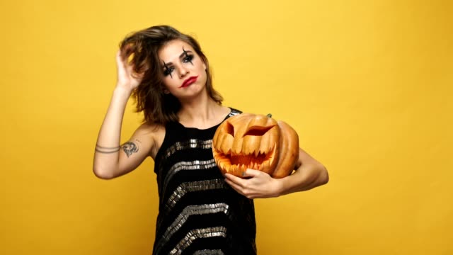 Young-pretty-funny-lady-with-scary-make-up-hugging-with-pumpkin-isolated-over-yellow
