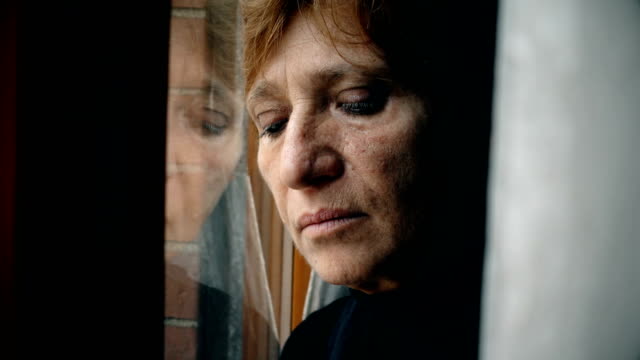 Close-up-on-sad-and-depressed-mature-woman-leaning-against-the-window