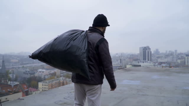 Homeless-with-garbage-bag-walks-at-the-roof-of-abandoned-building