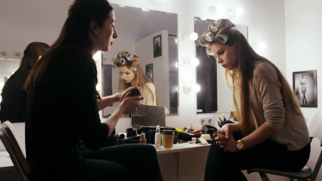 Frau-Schauspielerin-mit-Lockenwicklern-auf-Kopf-Kosmetik-mit-Make-up-Artist-zu-diskutieren