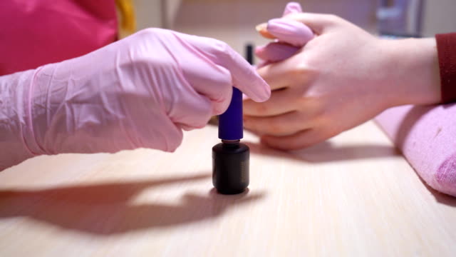 the-manicure-master-paints-the-client-nails-with-nail-polish.-beauty-saloon.-soft-focus.-Basque-with-nail-varnish-close-up.-4-k